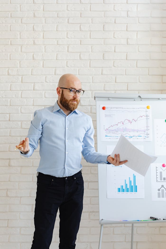 Bald businessman in corporate attire presenting charts during meeting indoors.